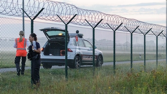 Eine Mitarbeiterin (l) der Flughafensicherheit des Flughafen Berlin-Brandenburg BER spricht mit einer Bundespolizistin am Zaun des Flughafens.