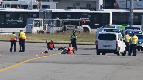 Einsatzfahrzeuge von Polizei, Feuerwehr und Flughafen-Sicherheit stehen auf dem Vorfeld des Frankfurter Flughafens, wo sich zwei Aktivisten (M) festgeklebt haben. 