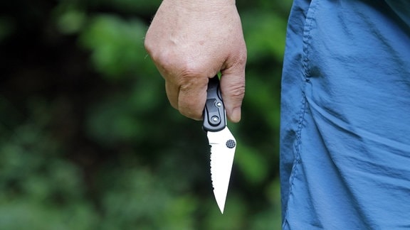 Eine männliche Hand hält ein gezacktes Messer.