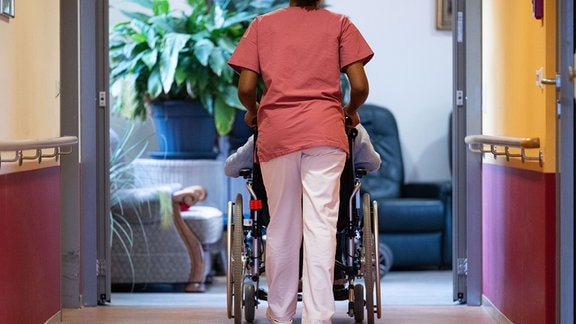 Eine Bewohnerin eines Pflegeheims wird von einer Pflegerin einen Gang entlang geschoben