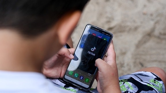 Ein Junge hält 2020 ein Smartphone in den Händen, auf dem das Logo der Kurzvideo-App TikTok zu sehen ist.