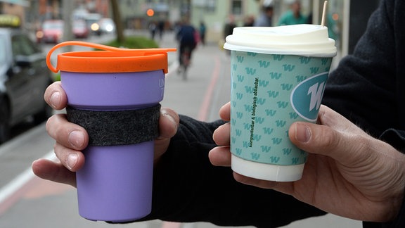 Ein Mehrweg-Kaffeebecher (l) und ein Einweg-Kaffeebecher werden nebeneinander gehalten. 