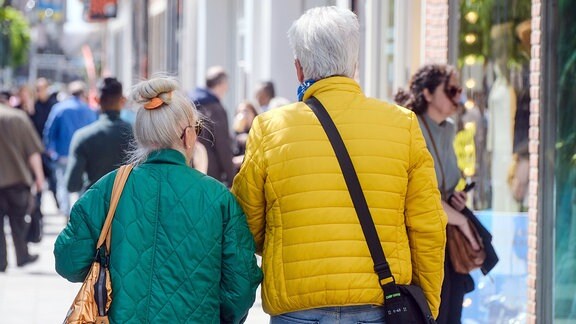 Rentner und Rentnerin laufen in Fußgängerzone einer Innenstadt.