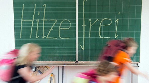 Schüler rennen an einer Wandtafel vorbei, an der groß Hitzefrei angeschrieben steht.