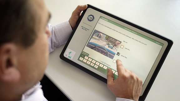 Ein Mann bedient ein Tablet, auf dem ein Programm zur Führerscheinprüfung läuft.
