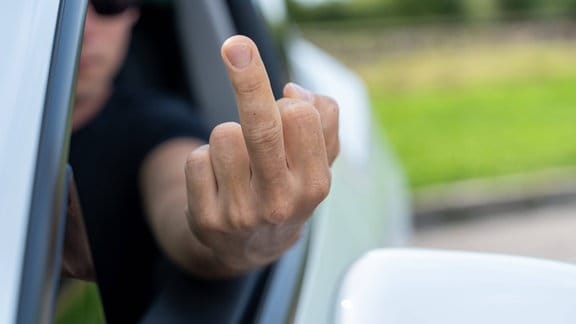Wütender Autofahrer zeigt einen Mittelfinger als Beleidigung im Straßenverkehr