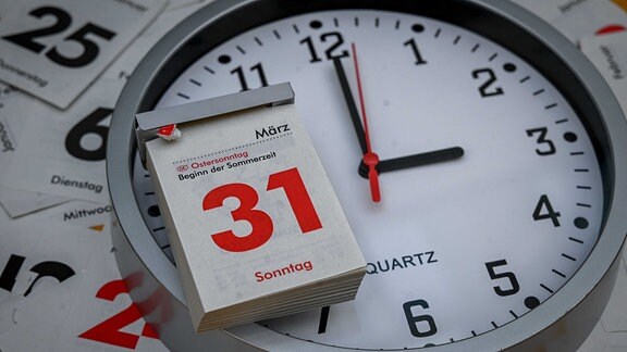 Ein Abreißkalender mit dem Datum 31. März, Sonntag, liegt auf einer analogen Uhr, deren Ziffernblatt drei Uhr anzeigt.
