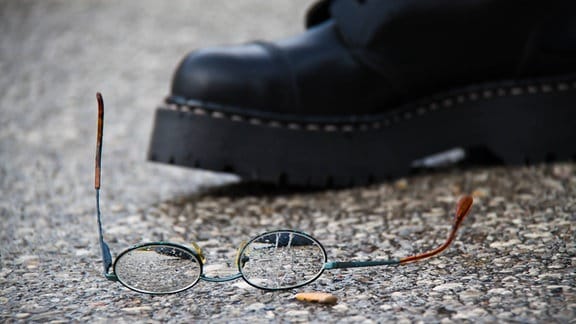 Zerbrochene Brille neben Springerstiefeln liegt auf dem Boden