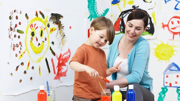 Eine Frau hockt neben einem malenden Kind.