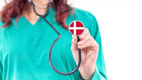 Medizinerin hält Stethoskop mit dänischer Flagge.