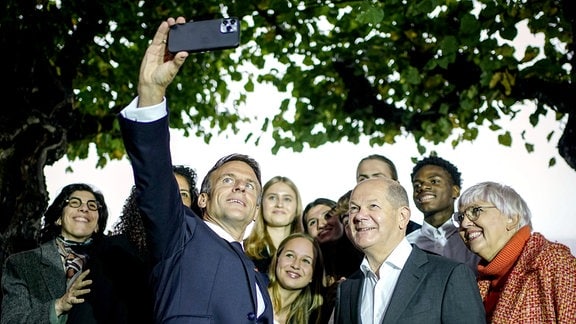 Bundeskanzler Olaf Scholz (M, SPD) und Emmanuel Macron (l), Staatspräsident von Frankreich, fotografieren ein Selfie während der Präsentation der App “KulturPass” im Hotel Louis C. Jacob neben Claudia Roth (r, Bündnis 90/Die Grünen), Staatsministerin für Kultur und Medien.