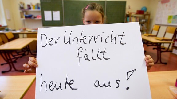 Ein Schild "Der Unterricht fällt heute aus!" wird in Osnabrück im Klassenraum einer Grundschule von einer Schülerin gehalten. 