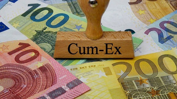 Auf Geldscheinen steht ein Stempel mit dem Schriftzug Cum-Ex.