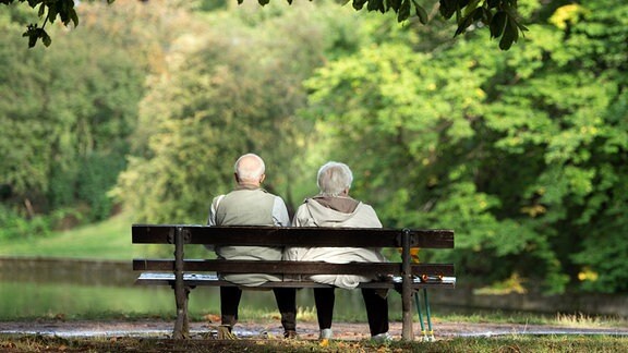 Zwei Senioren sitzen auf einer Bank im Grünen. 