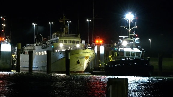 Im Dunkeln: Ein Schiff wird von zwei Sckeppern in einen Hafen gezogen. 