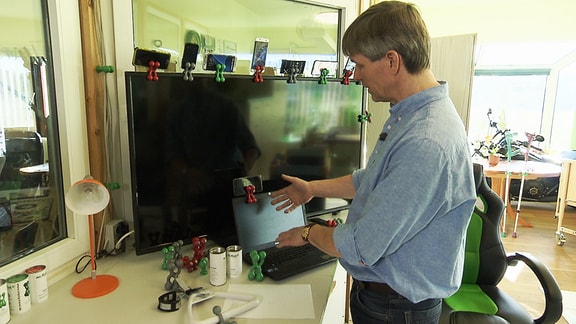 Ein Mann zeigt in seinem Büro verschiedene Versionen des sogenannten "Gnubbel" einer Halterung aus farbigem Silikon.
