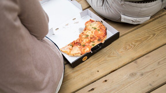 Zwei junge Frauen sitzen auf einem Steg in einem Park in Hamburg und essen eine Pizza