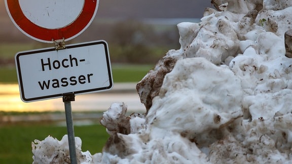 Neben einem Schneehaufen steht an der Donau ein Schild mit der Aufschrift "Hochwasser"