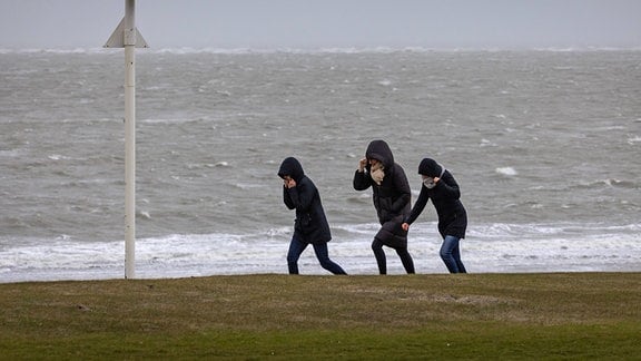 Spaziergänger kämpfen auf der Strandpromenade von Norderney gegen den Wind