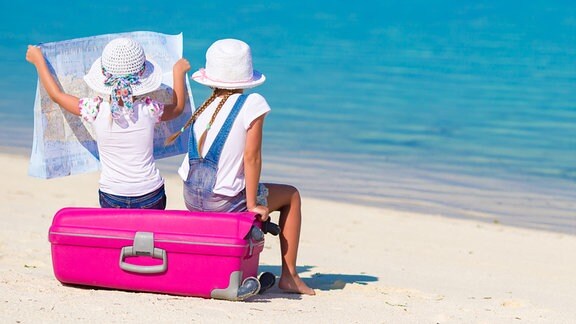 zwei Mädchen sitzen auf einem pinken Koffer und betrachten eine Landkarte