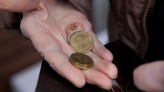 Eine aeltere Frau hält Kleingeld und ein Portmonnee in der Hand.
