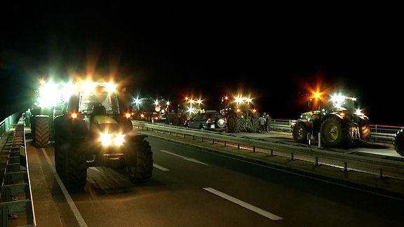 Mehrere Traktoren auf einer Autobahnbrücke im Dunkeln