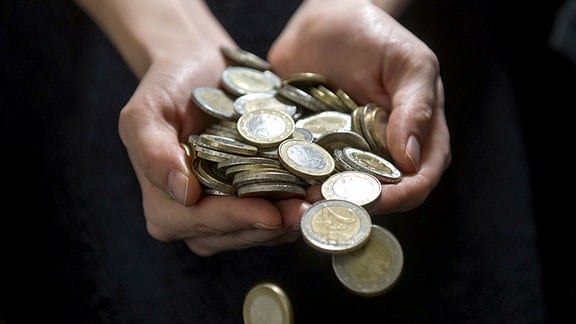 Eine Frau hält zahlreiche Münzen in den Händen und lässt diese auf den Boden fallen