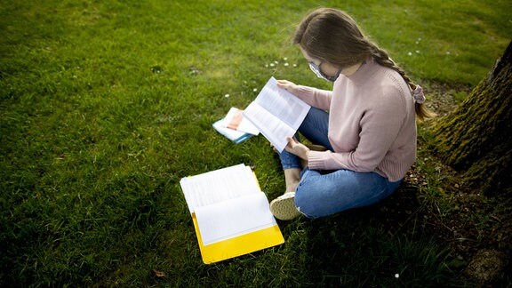 Junge Studentin sitzt an einem Baum im Freien und lernt.
