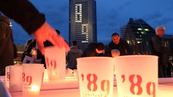 Menschen stellen auf dem Augustusplatz Kerzen mit der Aufschrift "'89 - Lichtfest Leipzig" auf ein Podest