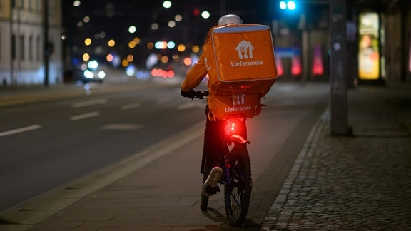 Ein Fahrrad Kurier des Lieferdienstes "Lieferando" fährt am Abend auf einem Radweg entlang.
