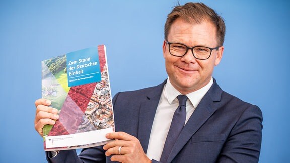 Carsten Schneider (SPD), Staatsminister und Ostbeauftragter der Bundesregierung, zeigt den Bericht zum Stand der Deutschen Einheit