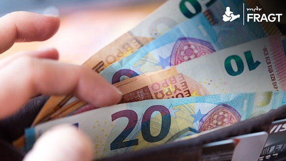 Eine Frau hält ein Portemonnaie in der Hand, in dem Geldscheine stecken.