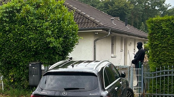 Ein Polizist steht vor einem Haus neben einem schwarzem Mercedes.