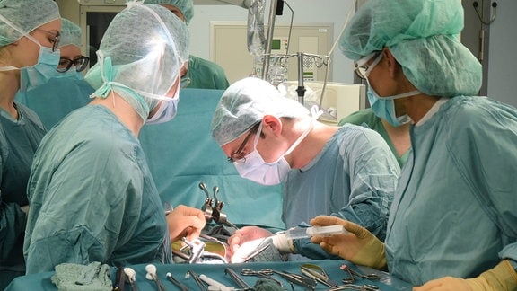 Operationssall mit 6 Personen die einer einer 7. Person operieren. 