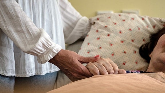 Eine Hand hält die Hand einer älteren Person im Bett.