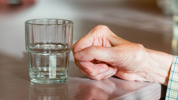 Die Hand einer Seniorin liegt neben einem Wasserglas.