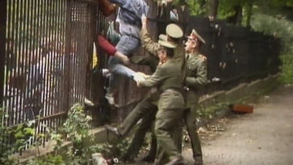 Menschen klettern über den Zaun der Botschaft der BRD in Prag, Soldaten versuchen sie daran zu hindern.