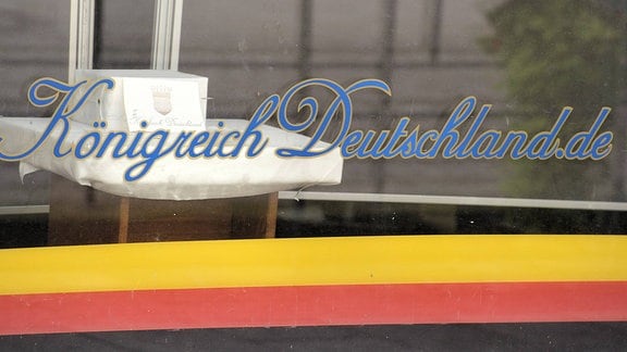 Schriftzug Königreich Deutschland.de auf der Schaufensterscheibe eines Ladengeschäftes in Lutherstadt Wittenberg; darunter die umgedrehten Farben der Deutschlandfahne.