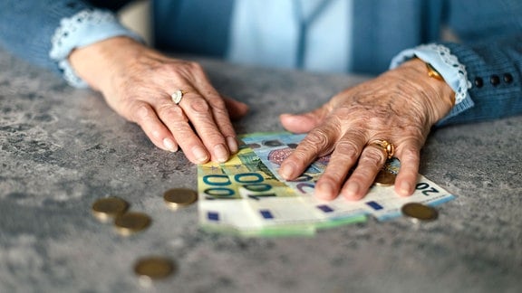 Seniorin zählt Geldscheine und Münzen auf einem Tisch.