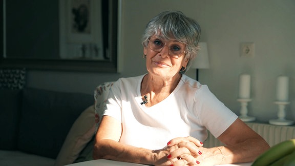 Eine ältere Frau mit Brille sitzt an einem Tisch