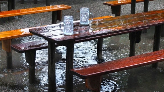 Zwei leere Gläser auf einem Tisch in einem leeren, regennassen Biergarten