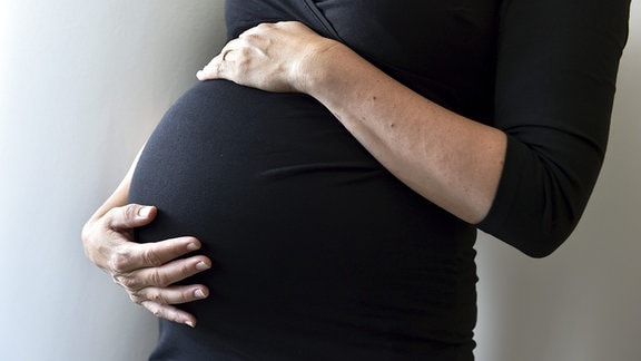 Eine schwangere Frau hält sich den Bauch. 
