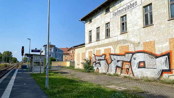 Ein verlassen aussehendes und mit Graffiti besprühtes Gebäude steht neben Bahngleisen.