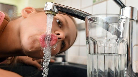 Ein Mädchen trinkt Leitungswasser aus einem Wasserhahn