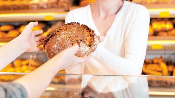 Verkäuferin überreicht ein Brot in einer Bäckerei.