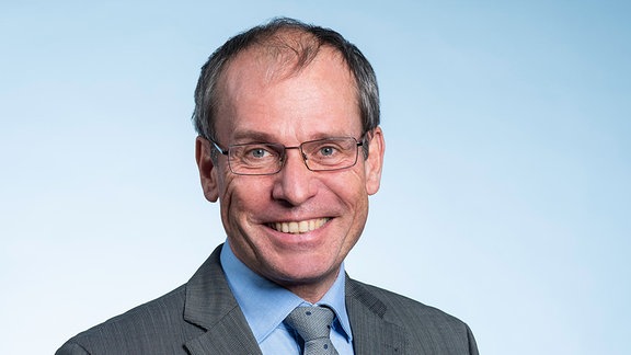 Bernd Fitzenberger: Mann, Ende 50. Er hat graue Haare, blau-graue Augen und trägt eine Brille mit dünnem silbernen Rand.