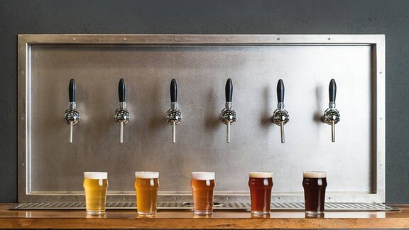 Symbolbild: verschiedene Biersorten im Glas jeweils unter einem Zapfhahn.