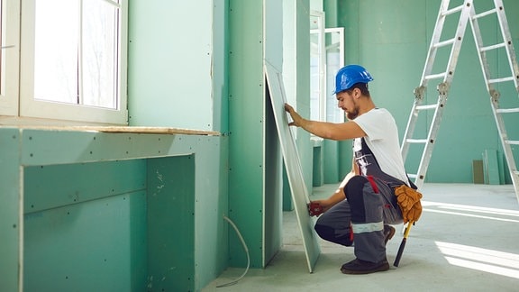 Bauarbeiter arbeitet mit Gipskartonplatten in einem Haus.