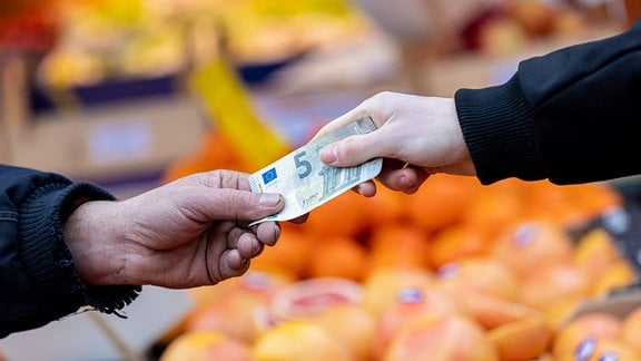 Ein Kunde bezahlt seinen Einkauf an einem Stand auf einem Wochenmarkt mit einem Fünf-Euro-Schein 