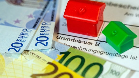 Illustration - Ein Spielzeughaus und die Nachbildung von Euro-Geldscheinen liegen auf einem Abgabenbescheid für die Entrichtung der Grundsteuer.